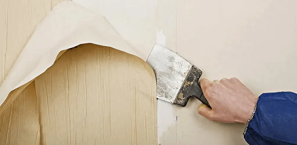 Handyman removing wallpaper with a scraper for wall preparation in Aurora, CO